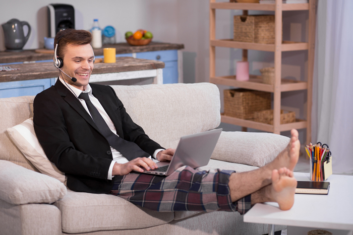 Male in jacket and pyjamas trousers on couch with laptop on his knees