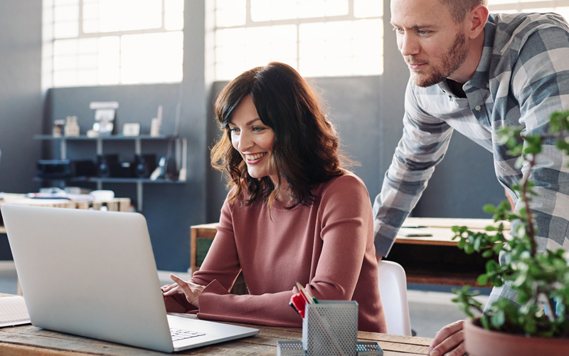 Woman working on a laptop with colleague offering support